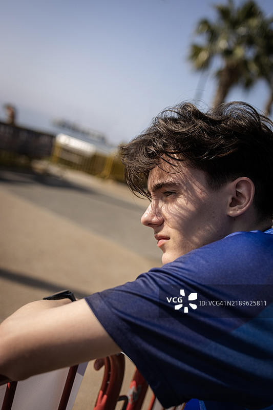 年轻男子坐在长椅上侧身望向远方图片素材