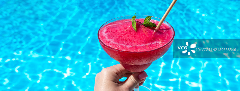阳光明媚的日子里，泳池旁拿着的冰冻红色饮料，夏季的概念图片素材