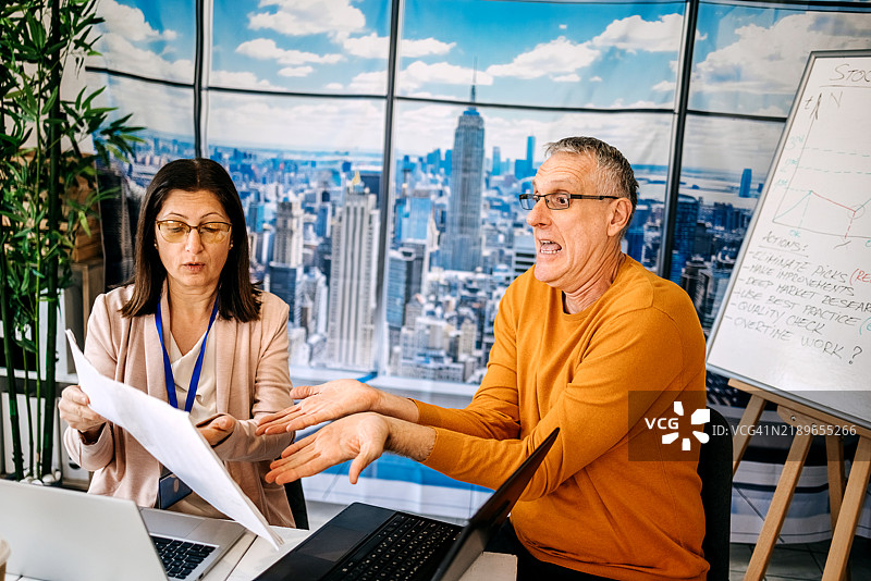 男性经理在工作中骚扰女性员工，同时查看笔记本电脑上的不良业绩。图片素材