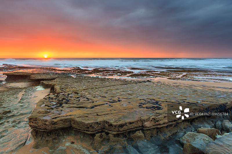 埃里塞拉海滩的海洋风景。色彩浓烈的爆炸性日落摄影。低潮时泡沫在岩石间翻滚，葡萄牙海景，里斯本地区。图片素材