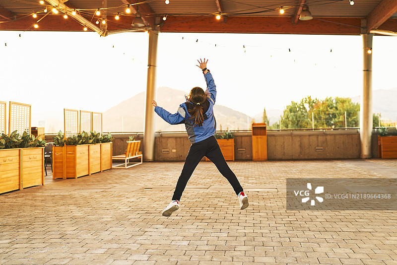 一个可爱的女孩穿着夹克，从后面跳跃，周围的餐厅里没有其他人。图片素材