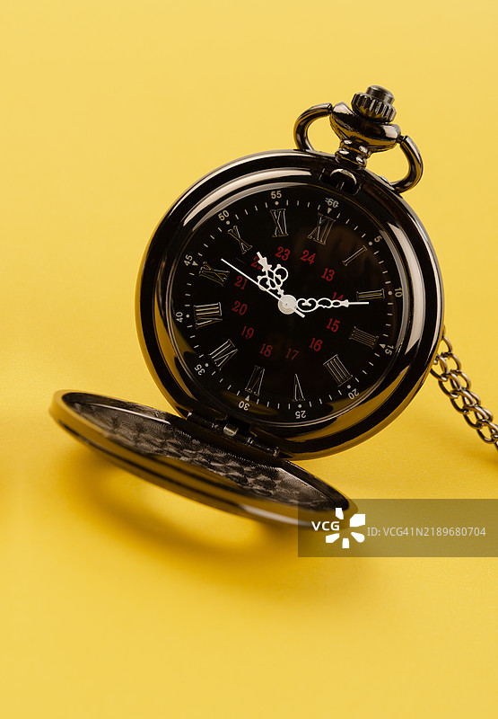 传统黑色怀表和链子在黄色背景上。图片素材