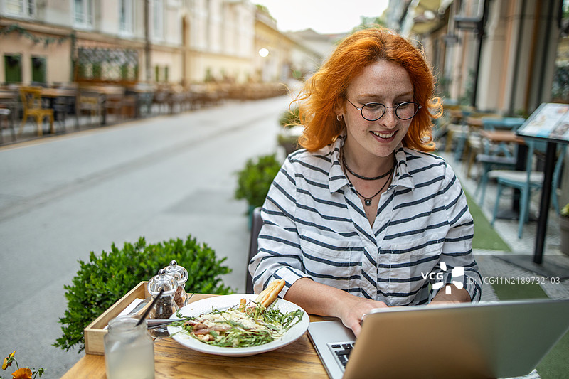一位高效的女性在户外咖啡馆享用午餐，同时在制作iStock作品集。图片素材