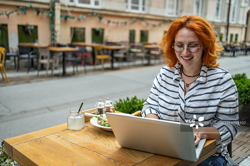一位高效的女性在户外咖啡馆享用午餐，同时处理她的iStock作品集图片素材