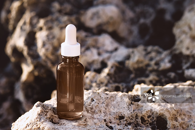 海边岩石上放着一瓶天然护肤化妆品的玻璃瓶。2025年流行的潘通色 - 摩卡色。图片素材