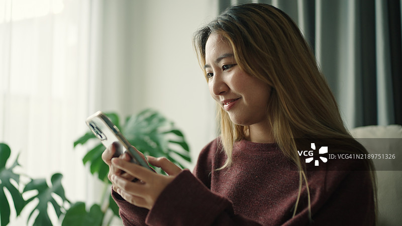女人在沙发上使用智能手机。图片素材