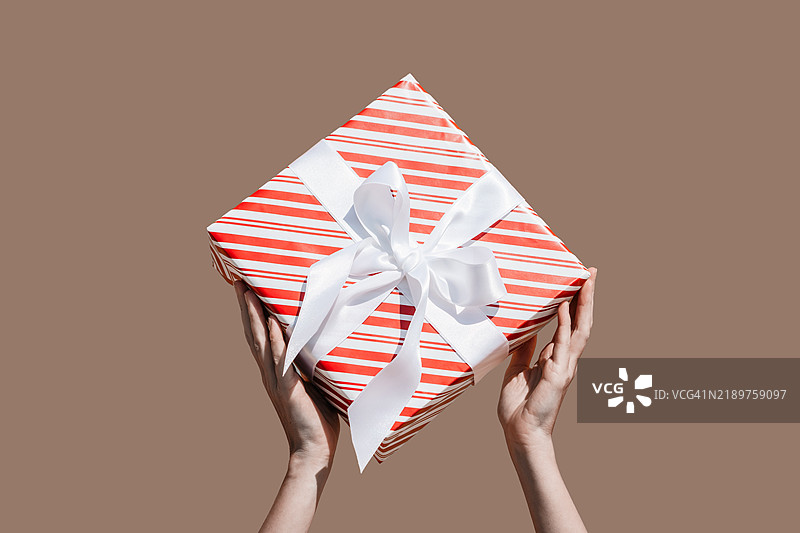 手握包裹着白色丝带的礼物，背景为棕色图片素材