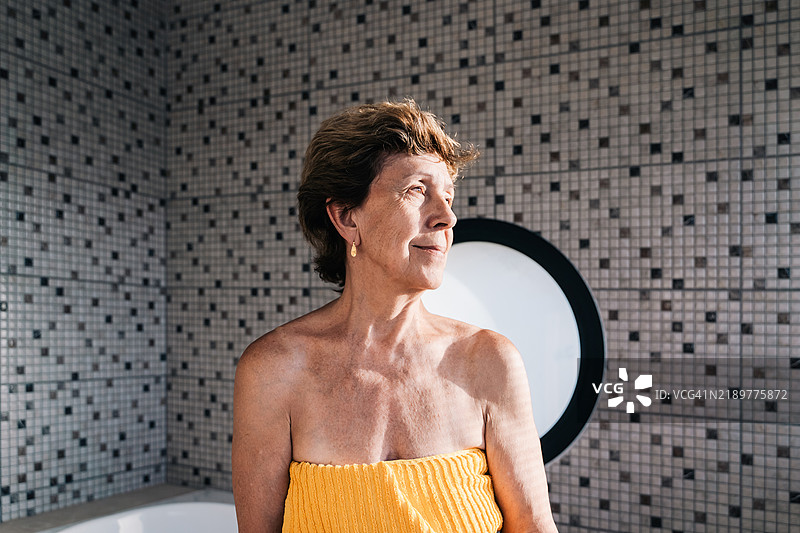 成熟的女性在时尚几何风格的浴室环境中用黄色毛巾沐浴图片素材