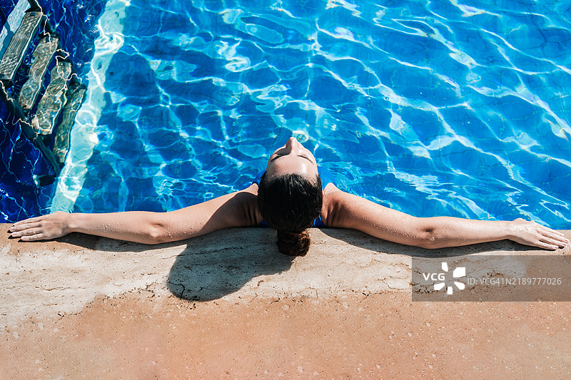 阳光明媚的日子里，女人在游泳池中放松身心图片素材