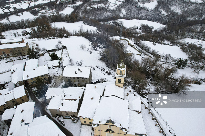 无人机拍摄意大利小村庄维佐拉卡的雪景，突出显示被雪覆盖的教堂和周围的房屋。图片素材