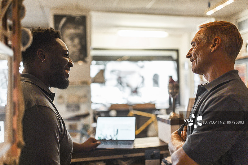 自行车店里，快乐的男性老板侧身与同事交谈图片素材