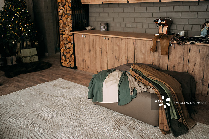 舒适的圣诞客厅里，沙发凳上摆放着衣物。图片素材