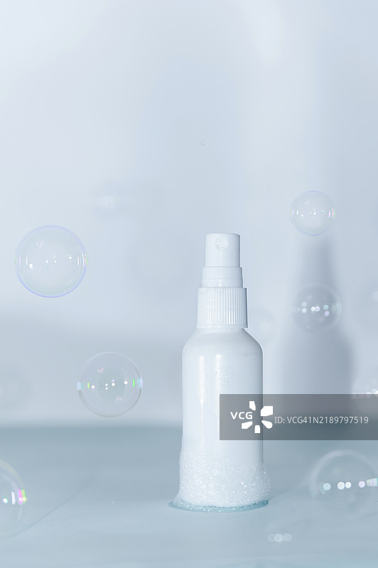 白色喷雾瓶被肥皂泡围绕，背景为浅色图片素材