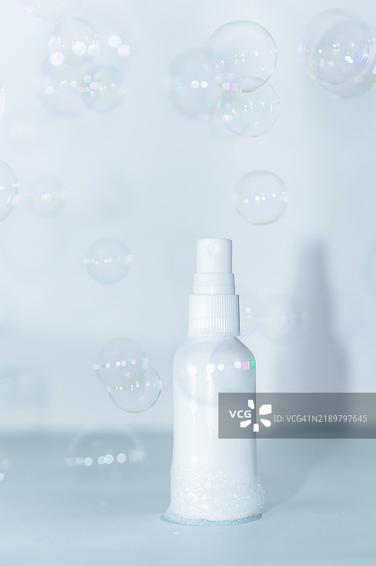 白色喷雾瓶被肥皂泡围绕，背景为浅色图片素材