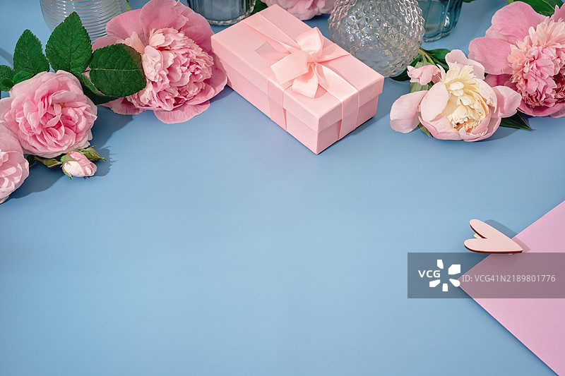 蓝色背景上的粉色玫瑰和牡丹花朵，带有心形的信封图片素材