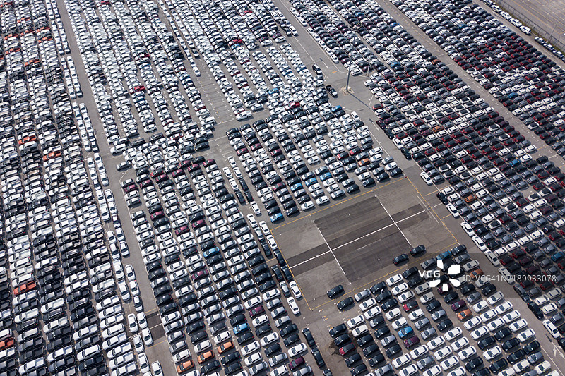 一处大型停车场的鸟瞰图，停满了整齐排列的新车，等待着它们的新主人。图片素材