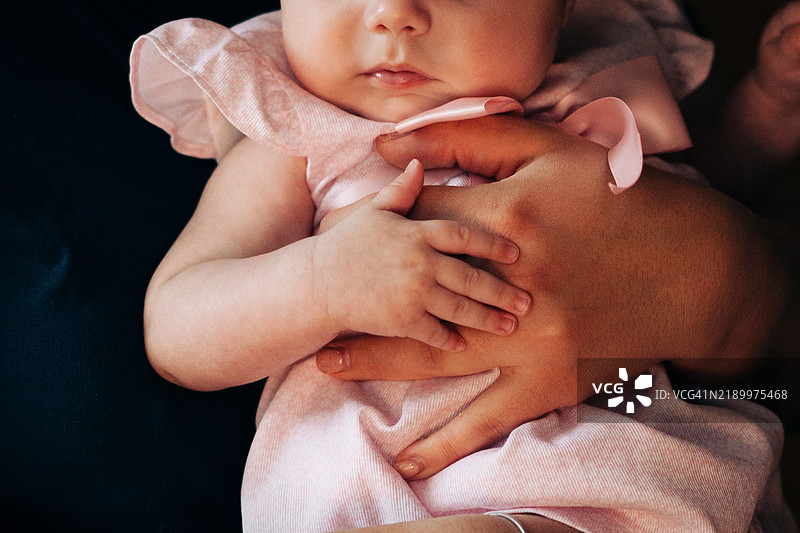 可爱的婴儿女孩穿着淡色裙子，被母亲抱着——温馨的家庭时刻图片素材