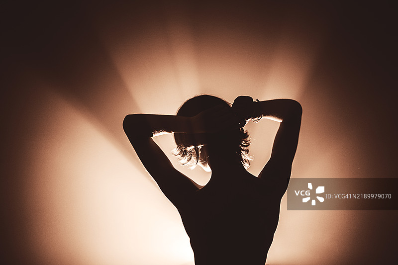 一位美丽的亚洲年轻女性，剪影在房间里随着电影灯光跳舞。2025年的色彩 - 摩卡棕和慕斯单色。图片素材