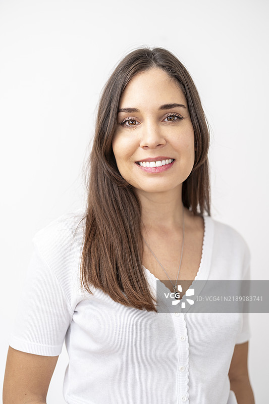 年轻的拉丁裔女性自信地微笑，展现自然美，穿着白色T恤的肖像。图片素材
