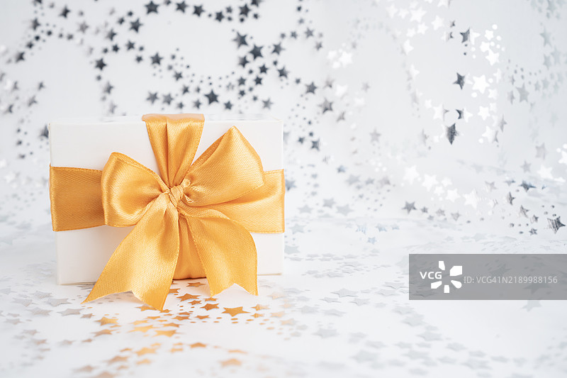 白色礼品盒上系着黄色丝带蝴蝶结，背景是银色闪光星星。图片素材