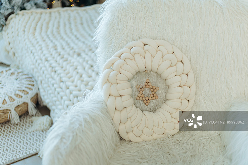 白色圆形针织靠垫放在毛茸茸的扶手椅上，前面是一条毯子，整个房间充满了圣诞气氛。图片素材