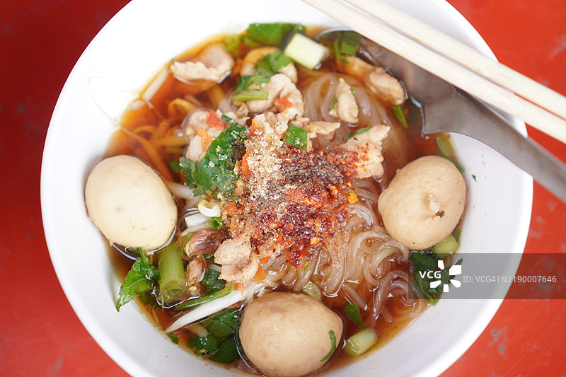泰式面条，白碗中盛着小面条、炖猪肉、肉丸、猪肝和血汤，搭配木筷和勺子，调味后美味的泰国菜。图片素材