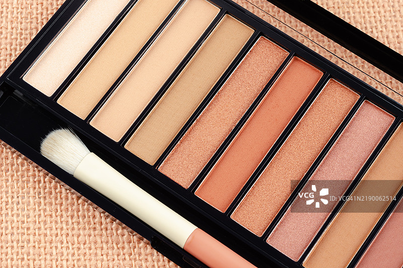 特写眼影盘和化妆刷，背景为麻布。眼影化妆品。图片素材