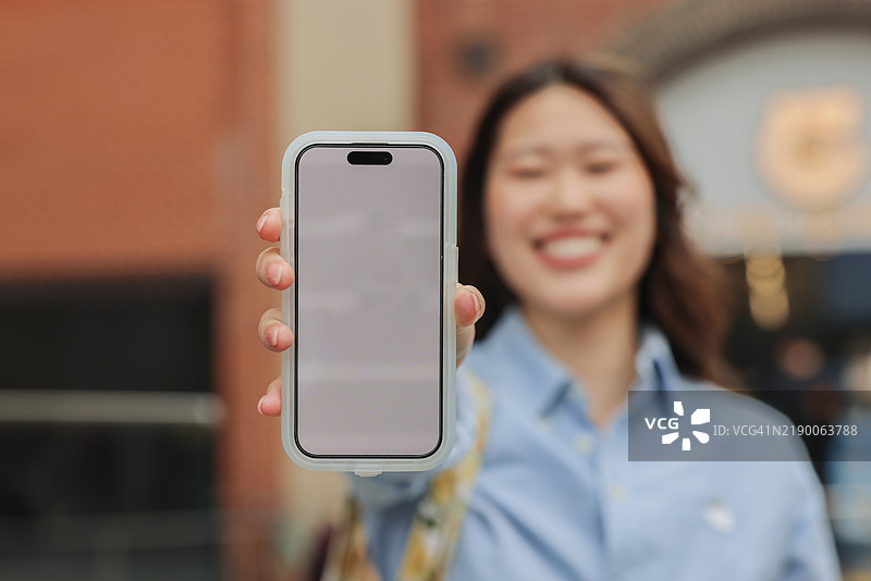 一位年轻女性在户外微笑着展示智能手机图片素材