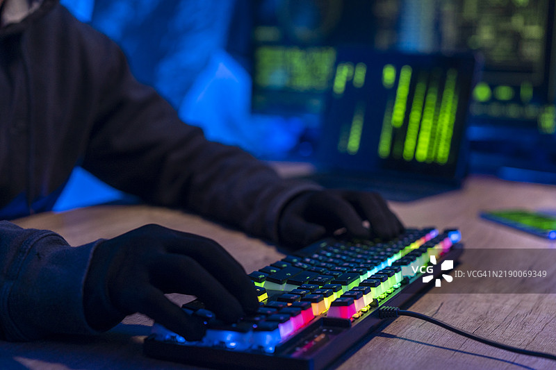 在黑暗的房间里，无法辨认的黑客的手部特写，正在桌子上用笔记本电脑键盘输入。图片素材