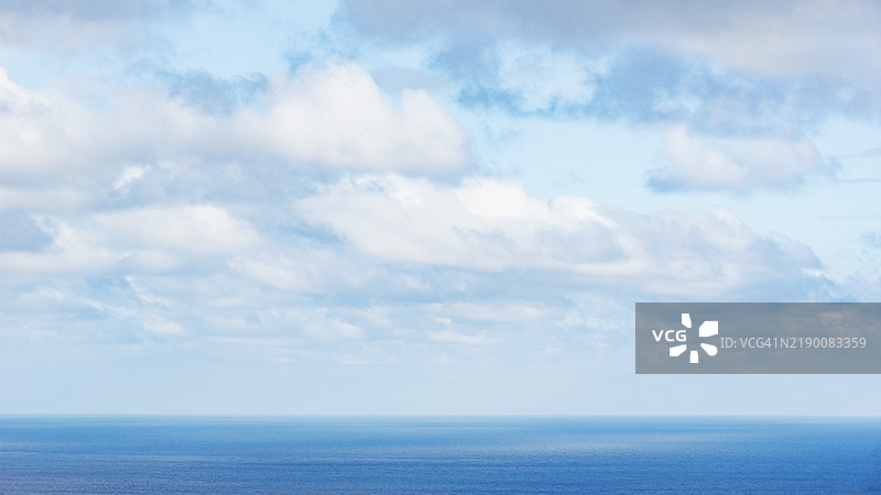 平静海面上方的白色蓬松云朵图片素材