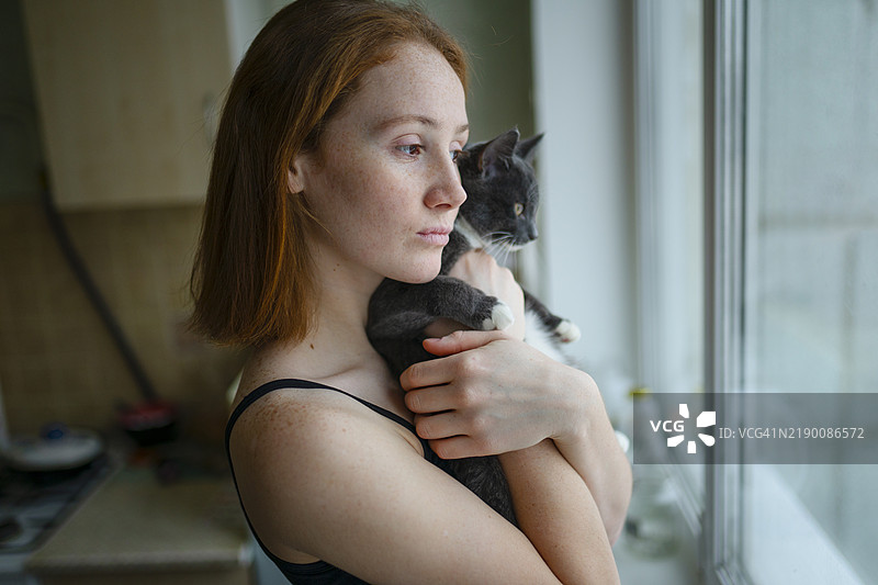 沉思的女人与猫一起透过窗户看外面图片素材