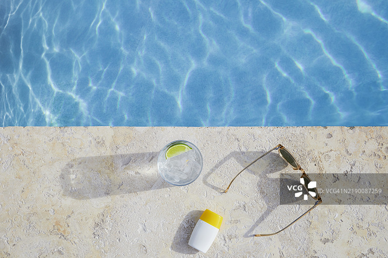 泳池边的太阳镜、防晒霜和饮料的俯视图图片素材