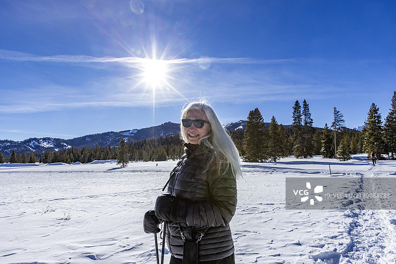 微笑的长白发女性在雪地里穿着雪鞋行走图片素材