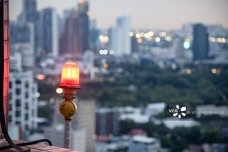 高层建筑屋顶安装的红色障碍灯，以确保飞行安全并警告飞机在红色警告灯城市景观背景下的危险。图片素材