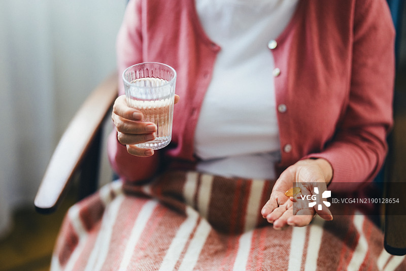 老年女性手持药物和水，进行日常健康护理图片素材
