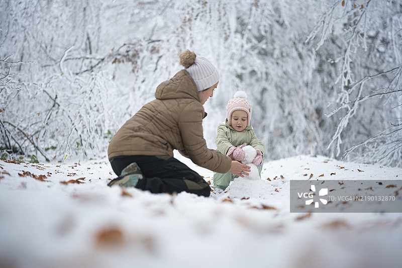 冬季家庭乐趣在雪林中。妈妈和孩子一起堆雪人图片素材