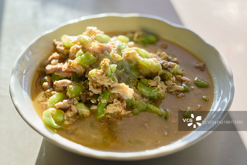 阳光明媚的台面上，白色盘子里的炒蛇瓜配猪肉和鸡蛋图片素材