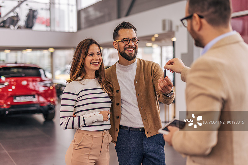 兴奋的情侣在新车经销商处领取钥匙。图片素材