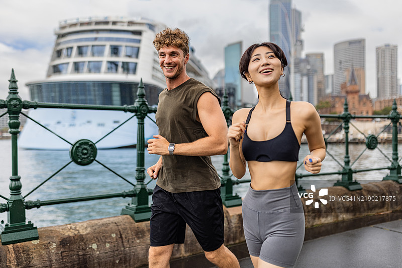 两个人在水边慢跑，背景是船只和城市景观图片素材
