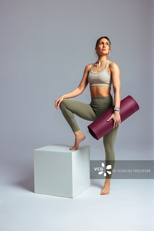 年轻的运动女性在工作室里手持瑜伽垫摆姿势图片素材