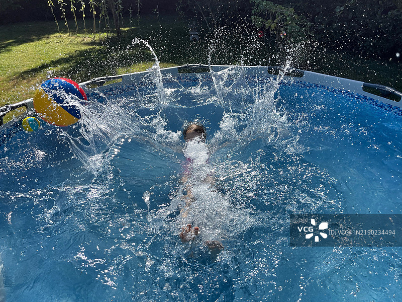 孩子在阳光明媚的夏日里向后扑入蓝色水池中。图片素材