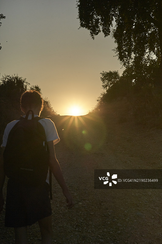 年轻男子在尘土飞扬的小路上行走，背景是葡萄牙的日落。图片素材