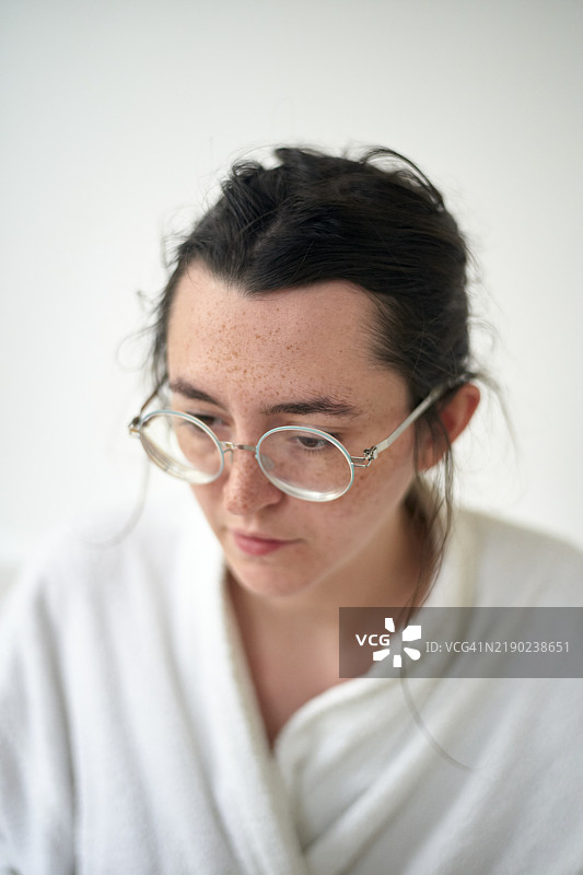 年轻女性戴着圆形眼镜，穿着白色长袍，沉思地低头。图片素材