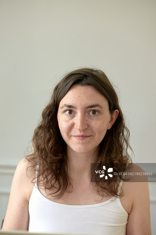 微笑着的雀斑女性，轻微抬头看着她的笔记本电脑，背景明亮。图片素材