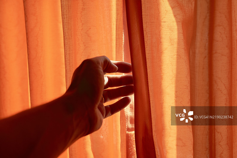 一只手正在拉开货船舱内的橙色窗帘，让阳光透进来。图片素材