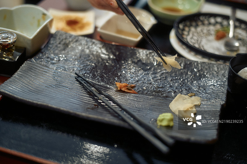 一盘凌乱的寿司特写，筷子和餐后残留物放在深色纹理盘子上图片素材