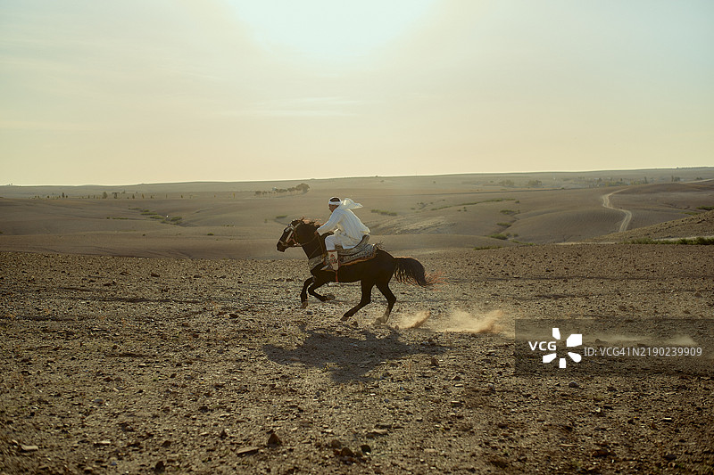 一个人在摩洛哥的广阔沙漠景观中黄昏时分骑马全速奔跑图片素材