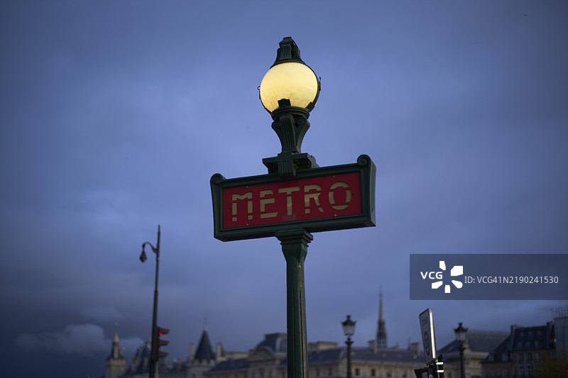 昏暗天空下，城市天际线剪影背景中的发光地铁标志图片素材