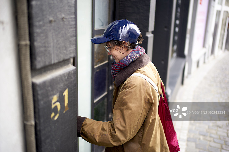 戴着蓝色闪亮帽子的年轻女性走进一栋标有51号的建筑。图片素材