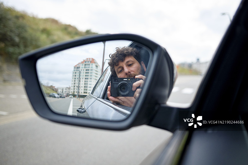 一个人在汽车侧镜中拍摄自己，背景是比利时的城市风景。图片素材